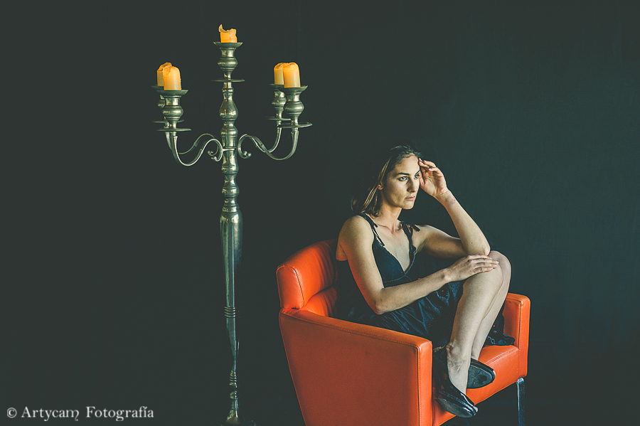 modelo chica pelo corto morena vestido negro luz velas candelabro gigante sofá naranja fondo negro